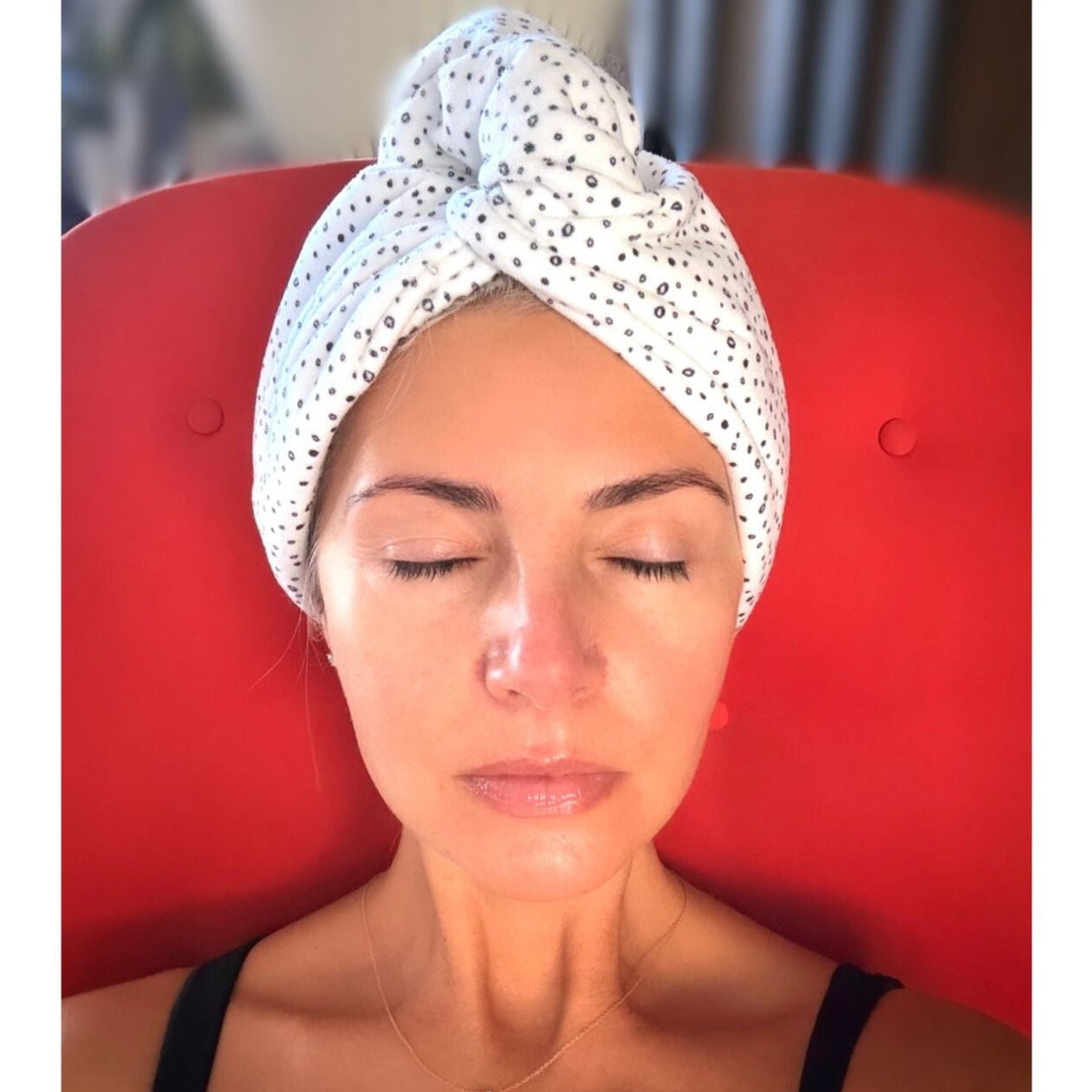 Woman with a towel wrapped around her head sitting on a red chair.